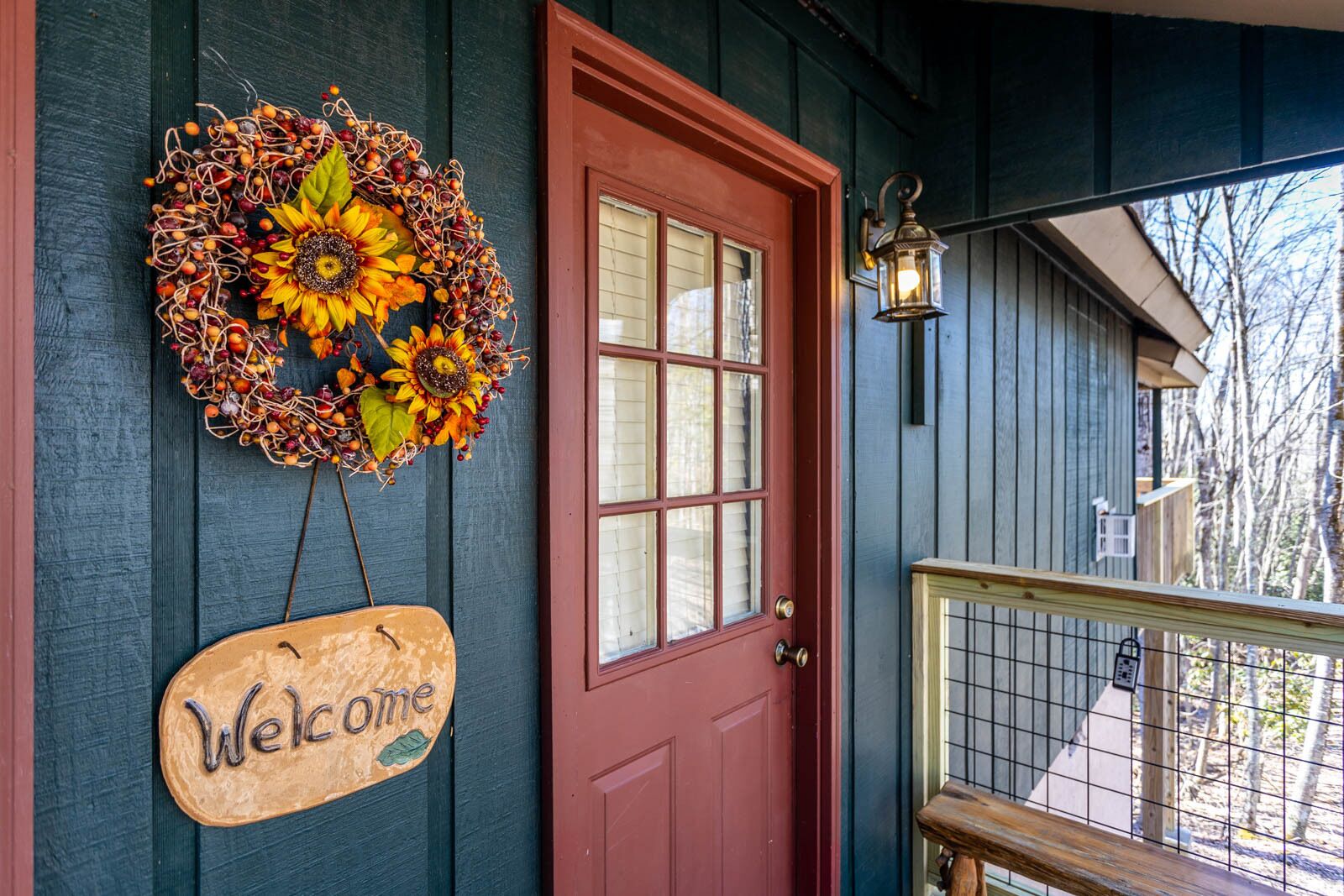 Een rode deur met een 'Welcome' bord, een decoratieve krans en een lantaarn op de veranda.