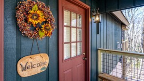 A red door with a 'Welcome' sign, a decorative wreath, and a lantern on the porch. - Peaceful Cabin Near Many Activities (Beech Mountain)