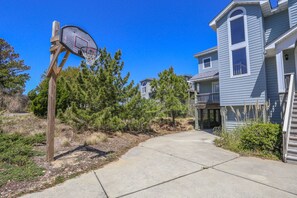 Un quartier résidentiel avec un panier de basketball, un chemin en béton et des maisons aux murs recouverts de bardage bleu et dotées d’un balcon.