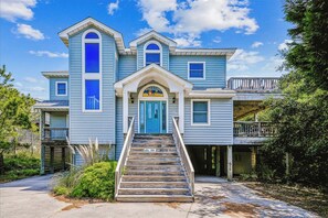 A two-story house with a blue exterior, a front porch, and a staircase leading to the front door. - All Ducks Go To Heaven - 6 BR Oceanside Home in Schooner Ridge w/Hot Tub (Duck)