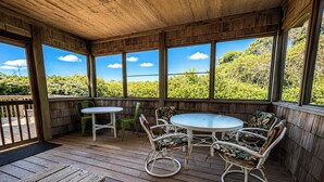 A wooden deck with a round table and chairs, large windows, and a view of greenery. - Garbee-Patt - 6 BR Semi Oceanfront home w/Private Pool & Ocean View (Southern Shores)