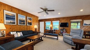 A wooden-paneled room with a sofa, armchairs, a coffee table, a TV, and a ceiling fan. - Garbee-Patt - 6 BR Semi Oceanfront home w/Private Pool & Ocean View (Southern Shores)