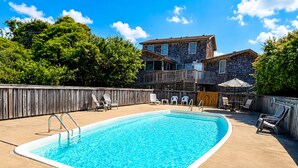 A rectangular swimming pool with a wooden deck, surrounded by a wooden fence, and a two-story building in the background. - Garbee-Patt - 6 BR Semi Oceanfront home w/Private Pool & Ocean View (Southern Shores)