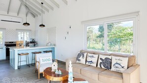 A modern kitchen with a bar area, a dining table with stools, and a sofa with decorative pillows. - Cozy cabin with océan view (Omoa)