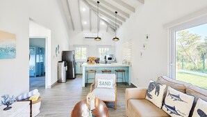 A spacious living room with a high ceiling, a kitchen with a central island, and a large window offering a view of the outdoors. - Cozy cabin with océan view (Omoa)
