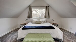 A bedroom with a sloped ceiling, a large bed with multiple pillows, a bedside table with a lamp, and a window with curtains. - Hyde Park Hyde Out Apt 5 (Boise)