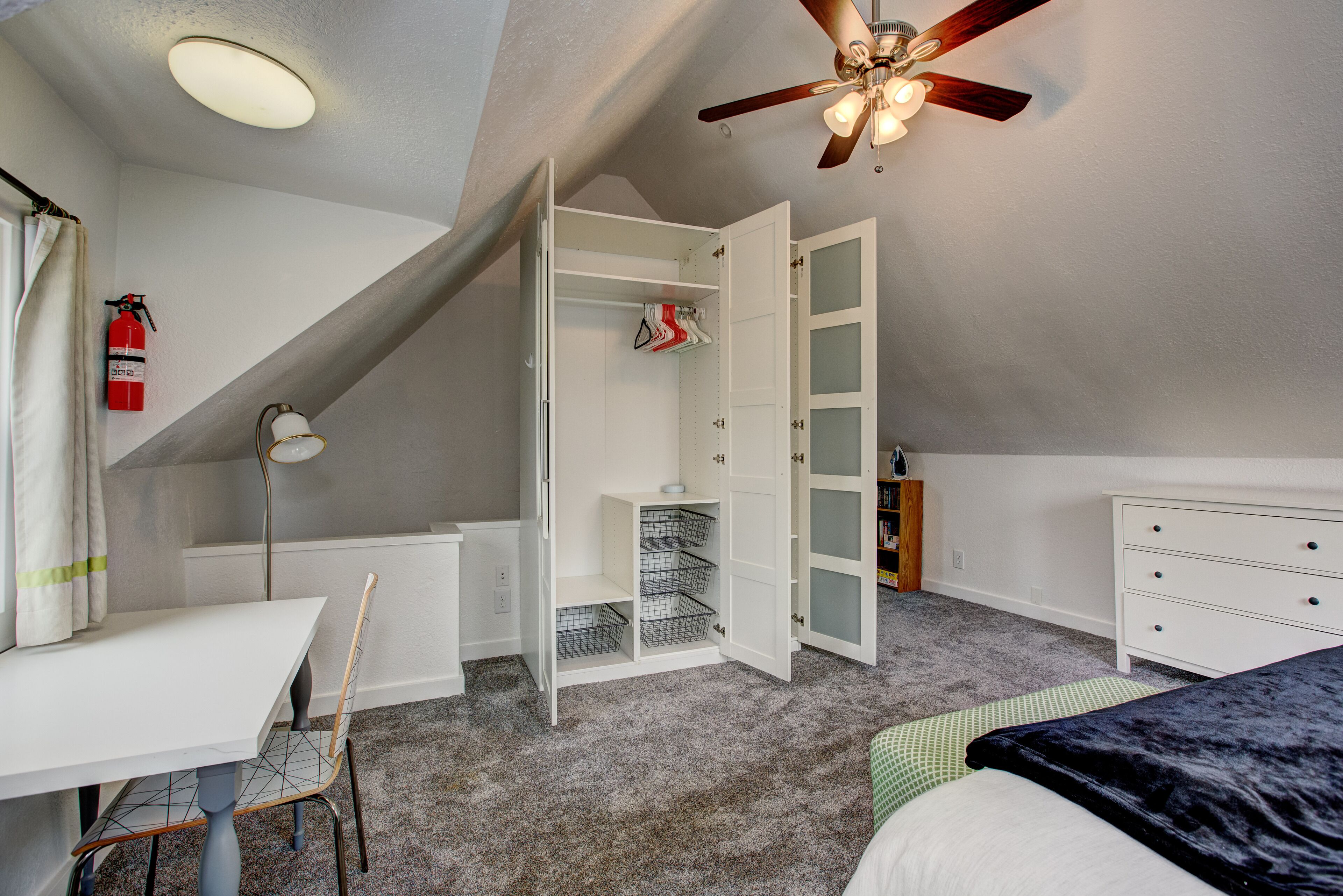 A bedroom with a sloped ceiling, a ceiling fan, a bed, a desk, and a closet.