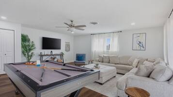 A living room with a pool table, a sofa, a television, and a ceiling fan.