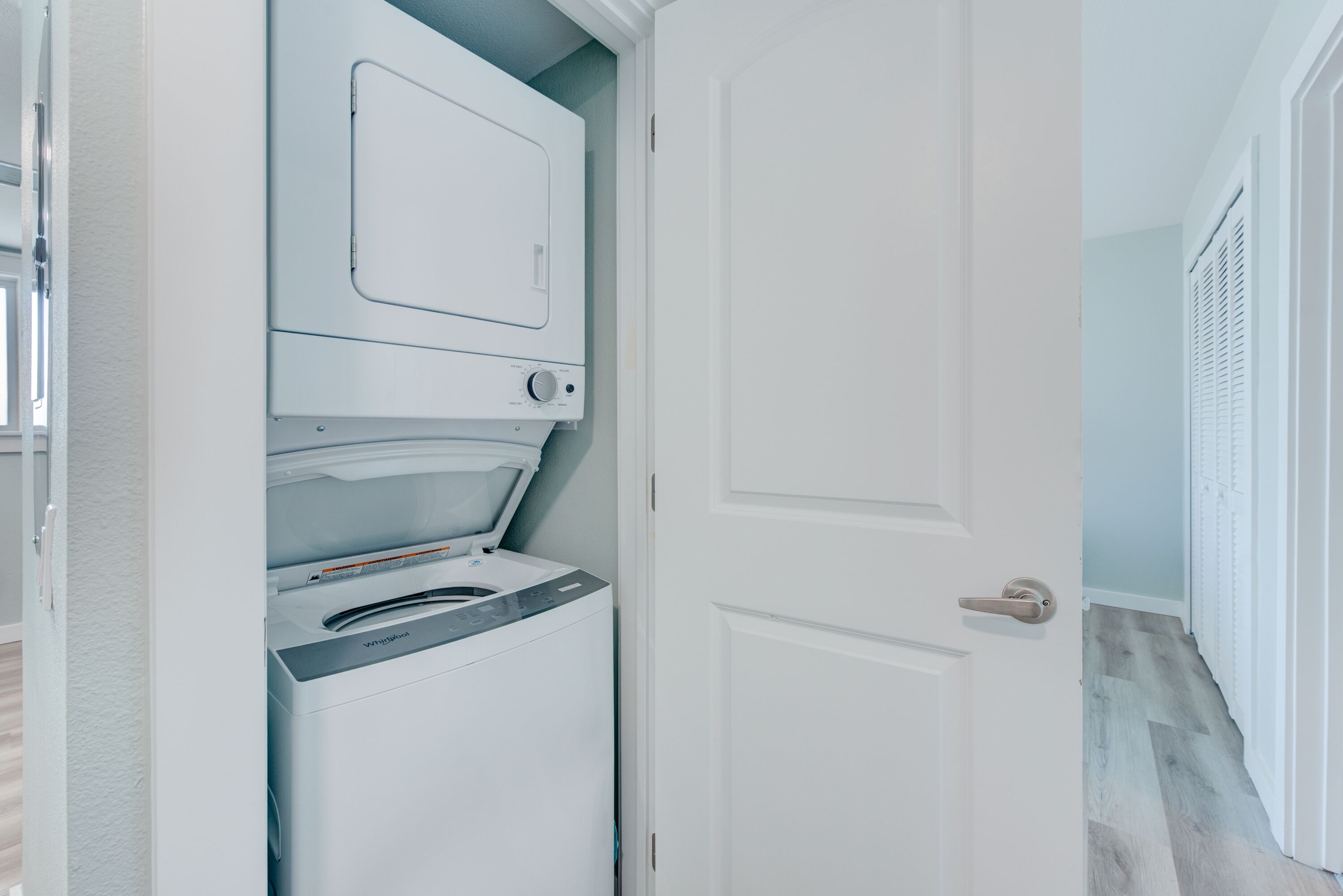A laundry room with a front-loading washer and dryer, a white door, and a herringbone-patterned floor.