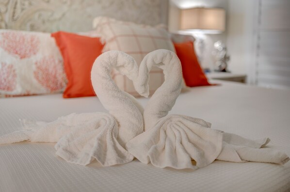 A bed with a white sheet and two towels arranged in a heart shape.