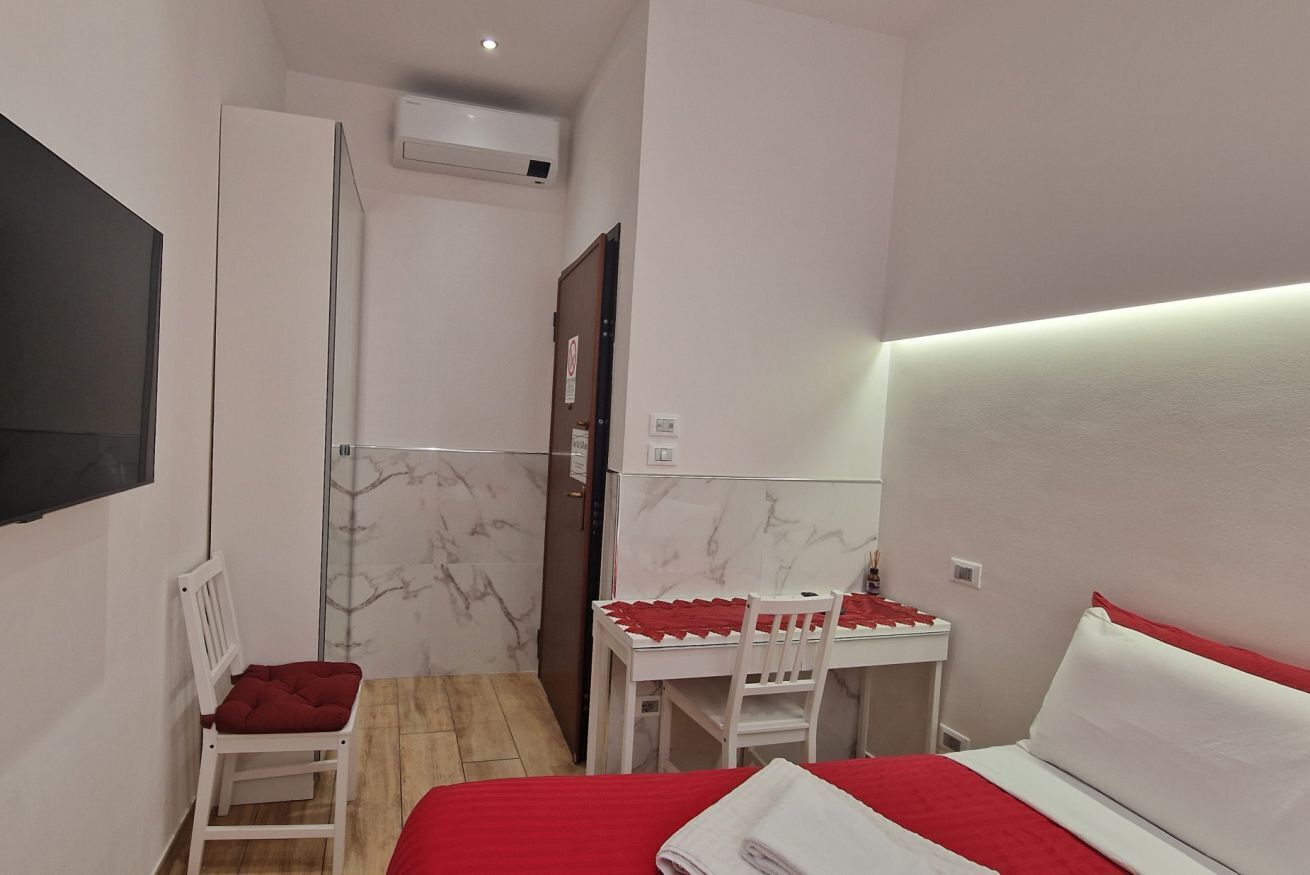 Habitación de hotel pequeña con cama, una mesita con sillas, televisor montado en la pared y zona de ducha.