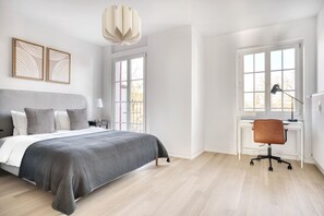 Une chambre moderne avec un grand lit, un bureau et une chaise. Elle comporte deux fenêtres et une porte.