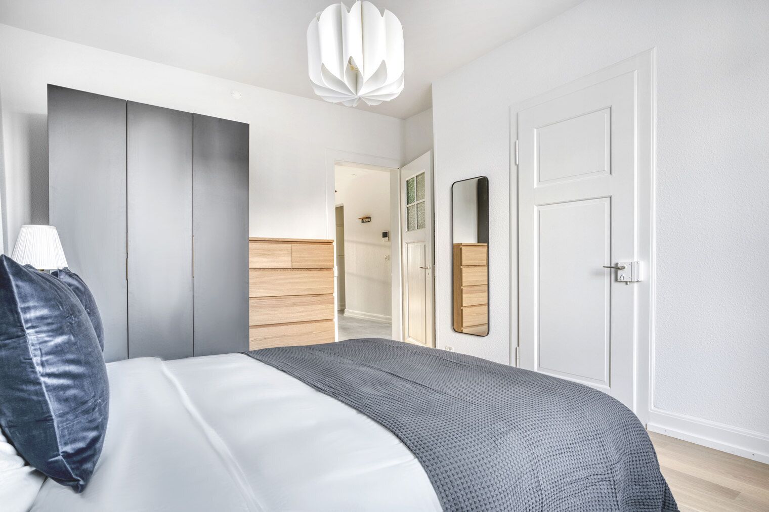A modern bedroom with a bed, a wardrobe, a mirror, and a door.
