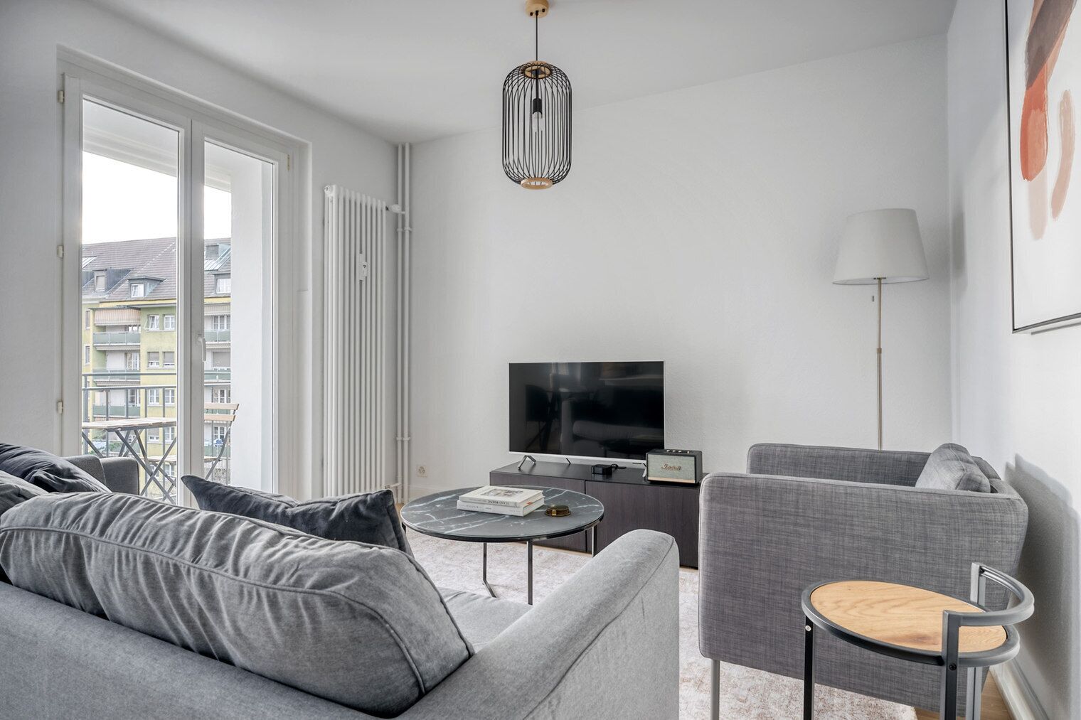 Un salon moderne avec un canapé gris, une petite table ronde, un téléviseur et une lampe.