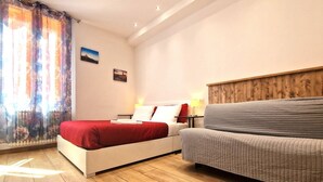 A bedroom with a bed, a sofa, a wooden headboard, a nightstand, and a window with curtains.