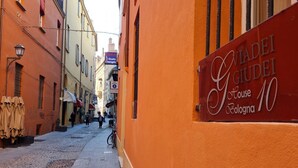 A narrow street with buildings on either side, one of which has a sign for "Giacomini Giudei House" in Bologna.