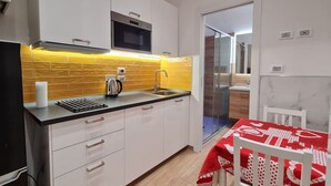 A compact kitchen with white cabinets, a black countertop, and a yellow-tiled backsplash.