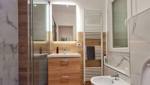 A modern bathroom with a glass shower enclosure, a wooden vanity with drawers, a white sink, and a towel rack.