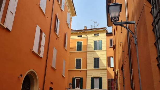 A narrow street with buildings painted in warm tones, featuring arched doorways and traditional shutters.