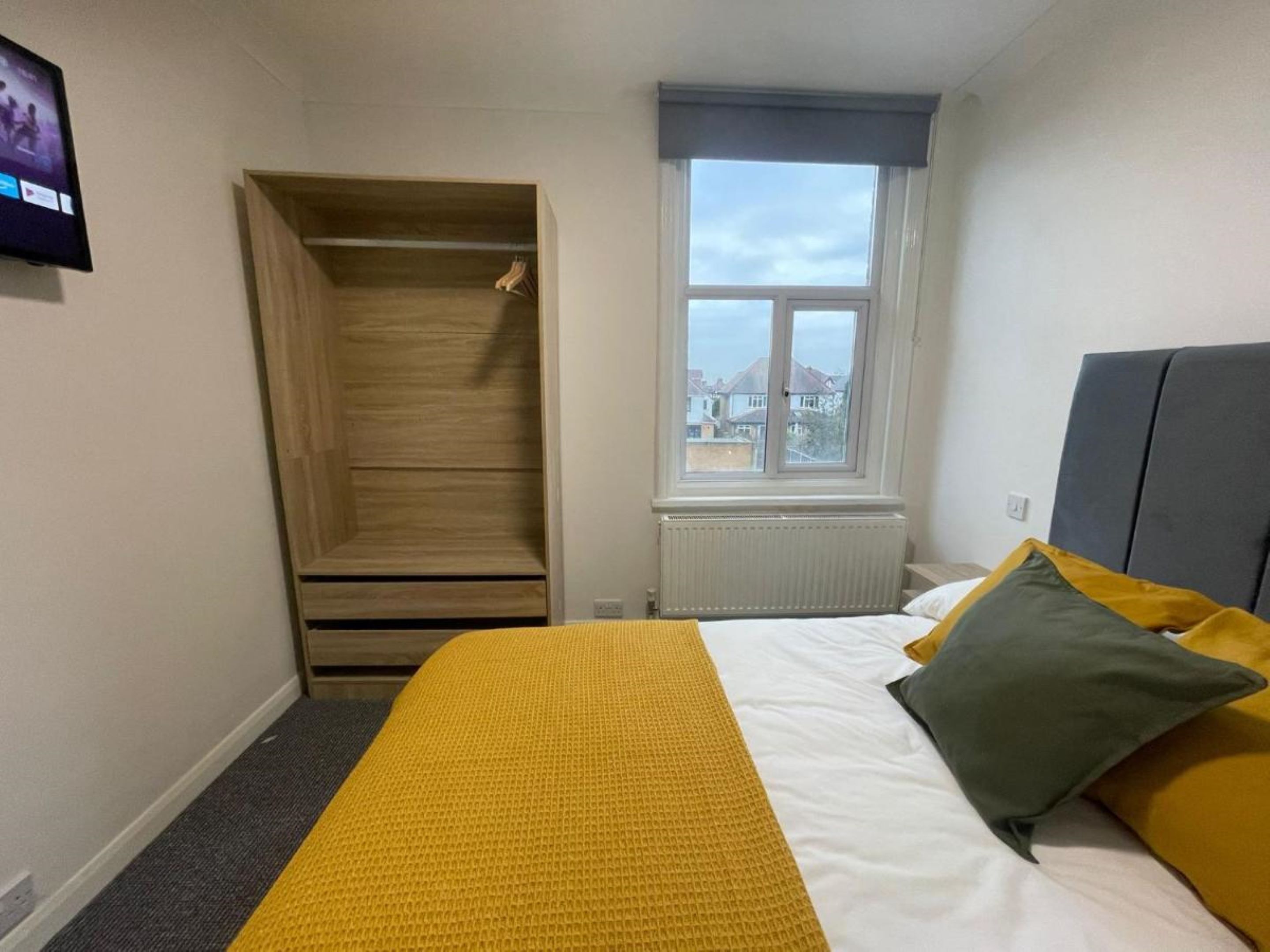 Ein Schlafzimmer mit Bett, Kleiderschrank, Fenster und Heizkörper.