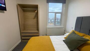 Ein Schlafzimmer mit Bett, Kleiderschrank, Fenster und Heizkörper.