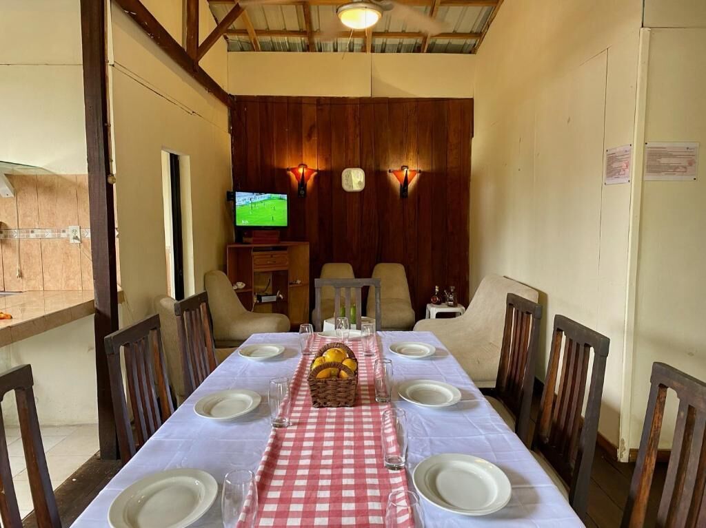 A dining area with a checkered tablecloth, wooden chairs, and a television in the background.