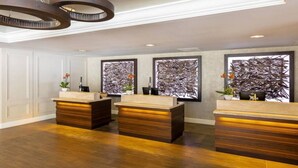 A reception area with three wooden reception desks, a modern chandelier, and abstract wall art. - Marriott Vacation Club Pulse, SF (San Francisco)