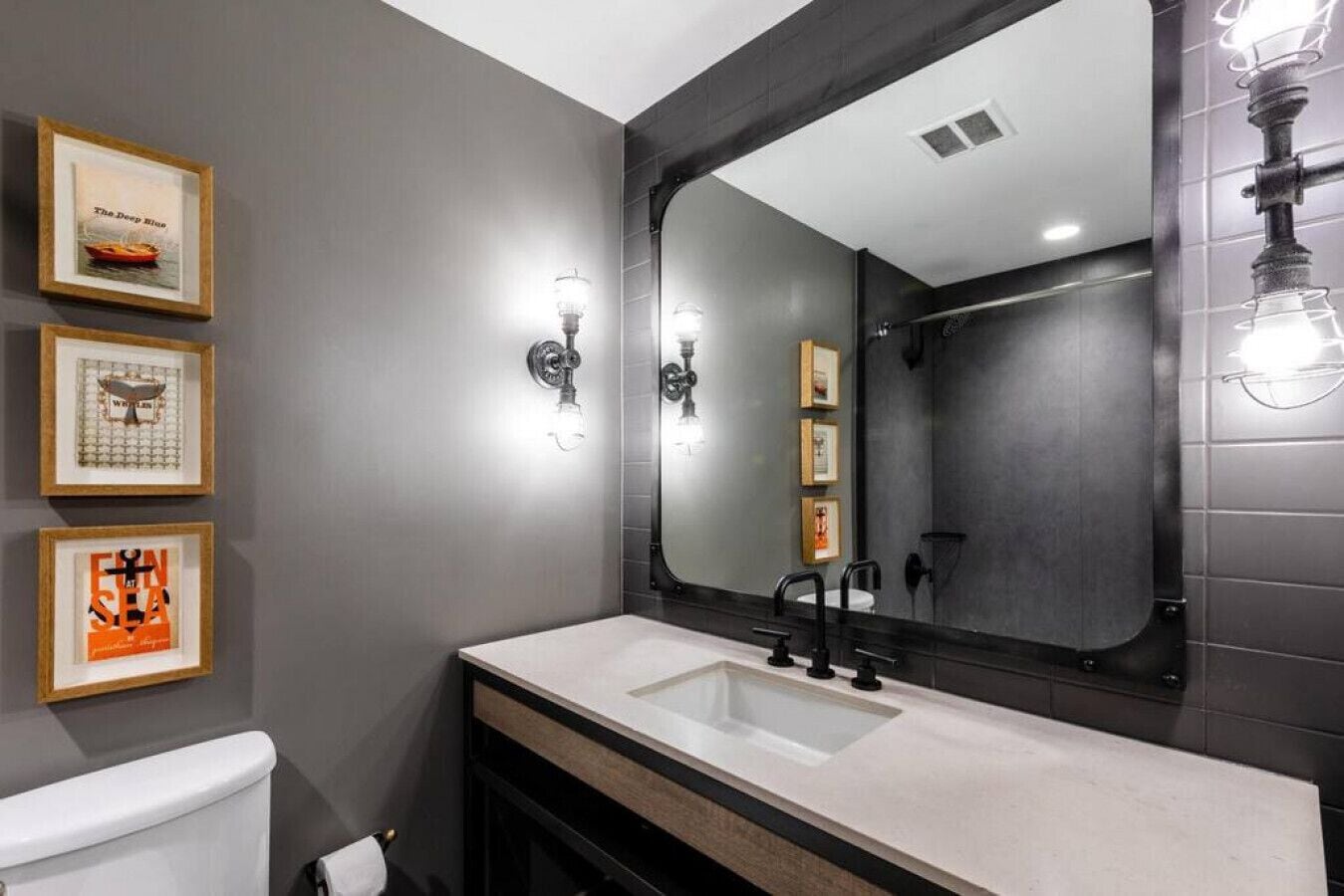 A modern bathroom with a large mirror, a white sink, and three framed pictures on the wall.
