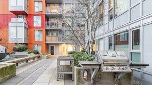 An outdoor patio with a barbecue grill, seating area, and a building with colorful exterior walls. - New Modern, Large 1 Bedroom, 1 Bathroom + Work Space (Vancouver)
