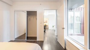 A hotel room with a bed, a wardrobe, a mirror, and a window. - New Modern, Large 1 Bedroom, 1 Bathroom + Work Space (Vancouver)