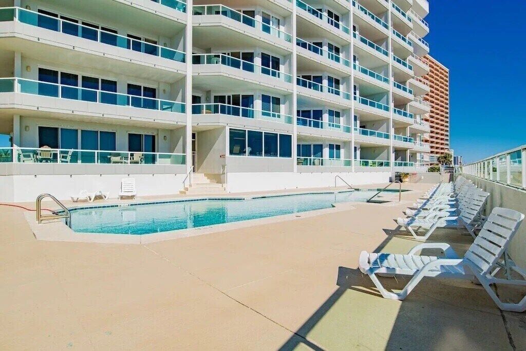 A multi-story hotel with a swimming pool and sun loungers.