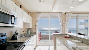 Une cuisine équipée d’une cuisinière, d’un four à micro-ondes et d’un évier, donnant sur un balcon avec vue sur la mer.