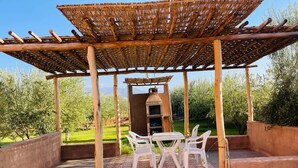 Un área de estar al aire libre techada, con piso de ladrillo y sillas de plástico blanco.