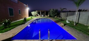 A swimming pool with a clear blue surface, surrounded by a well-maintained lawn and a brick building with windows.