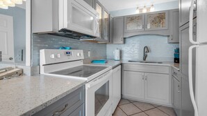 Una cocina moderna con electrodomésticos blancos, salpicadero de azulejos y encimera de granito.