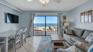 Una sala de estar con vista a la playa, un ventilador de techo, un televisor, un comedor y un sofá.
