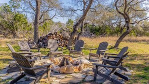 A stone fire pit surrounded by Adirondack chairs in an outdoor setting. - Sleeps 18, Ranch - Pool, Hot Tub, 2 Fire Pits (Dripping Springs)