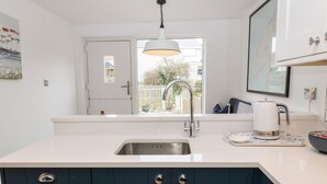 Une cuisine moderne avec un plan de travail blanc, un évier en acier inoxydable et des meubles de couleur bleu foncé.