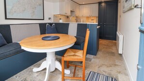 Un espace de vie compact comprenant une table à manger, un canapé, un fauteuil, une carte accrochée au mur et un coin cuisine.