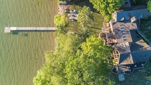 Vue aérienne d’une propriété au bord du lac, avec un quai, une maison dotée d’une terrasse et des arbres environnants.