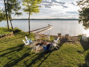 Terraza junto al lago con sillas Adirondack, una pequeña mesa y un bote.