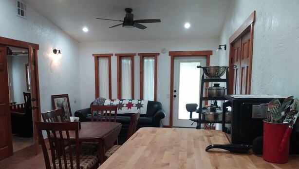 A dining area with a wooden table and chairs, a ceiling fan, and a kitchen area with a stove and utensils. - Studio in Pahrump | Death Valley NP (Pahrump)