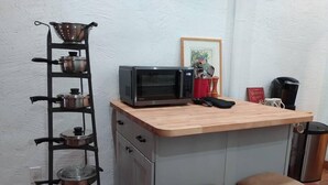 A compact kitchen with a microwave, a colander, and a pot rack. There are two stools and a coffee maker on the counter. - Studio in Pahrump | Death Valley NP (Pahrump)