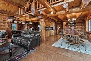 A log cabin interior with a leather sofa, dining table, and metal chairs.