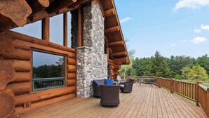 Eine Holzhütte mit einer Holzdachterrasse, einem Steinkamin und Gartenmöbeln.