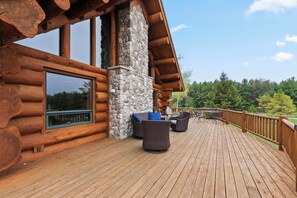 A log cabin with a wooden deck, stone fireplace, and outdoor furniture.