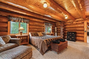 A log cabin bedroom with a bed, two lamps, a dresser, and a chair.