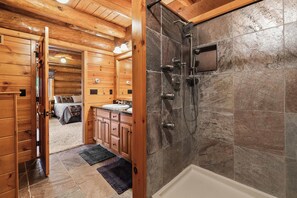 Interior de una cabaña de madera con baño que incluye ducha, lavamanos y armarios.