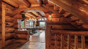 Ein Blockhaus-Interieur mit Steinböden, Holzbalken an der Decke und Blick durch ein Fenster.