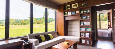 A modern living room with a large window, a sofa, a coffee table, and a bookshelf.